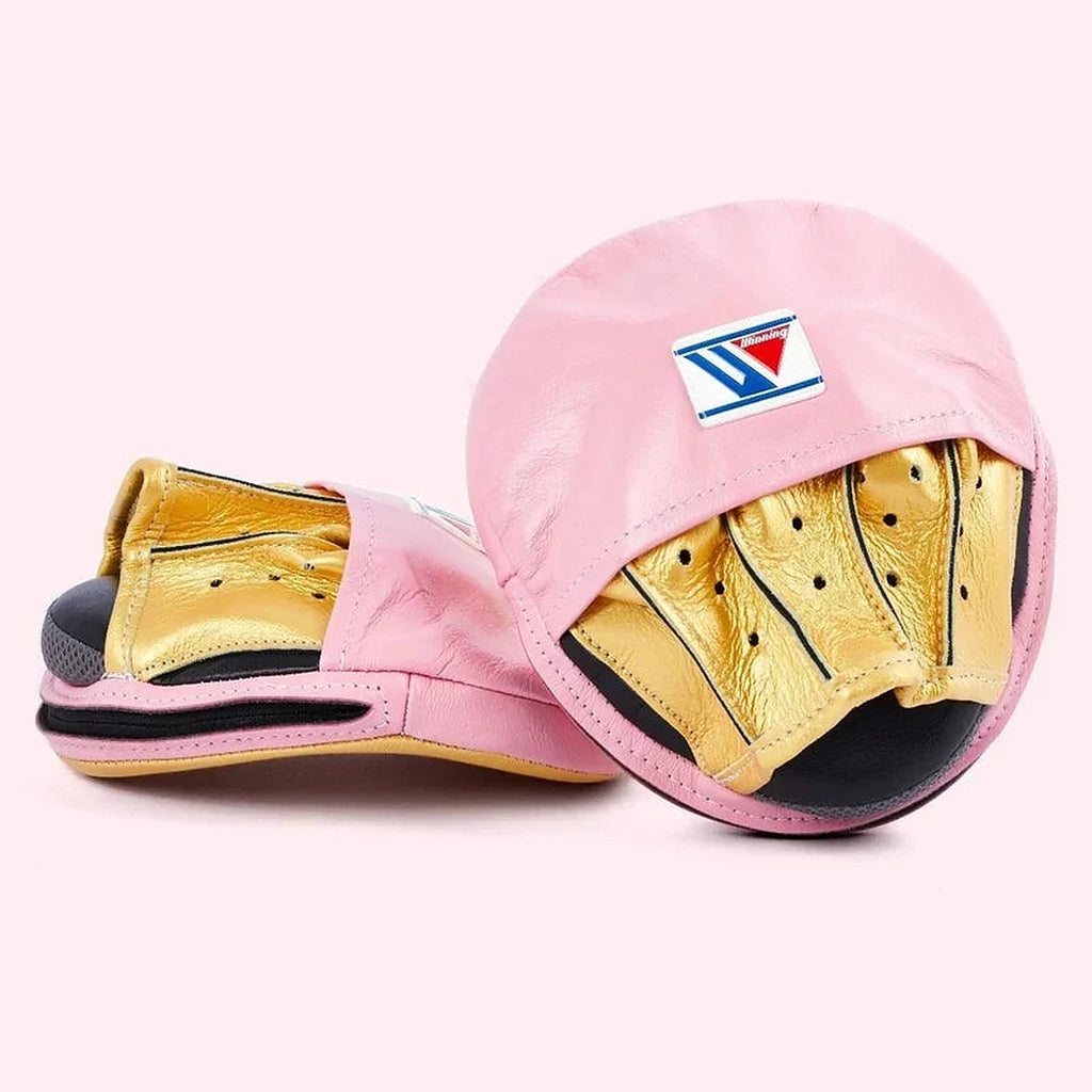 Winning pink curved focus mitts with shiny metallic gold grip on the palm side, shown as a matched pair - palm side